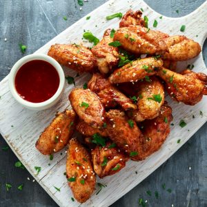 Baked chicken wings with sesame seeds and sweet chili sauce on white wooden board.